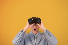 Surprised man looking through binoculars against yellow background Stock Image Surprised man looking through binoculars against yellow background Stock Image