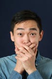 Surprised young Asian man covering mouth with palms