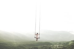 Surreal moment of a woman having fun on a swing hanging from the sky stock photo Surreal moment of a woman having fun on a swing hanging from the sky stock photo