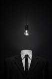 Surrealism and business theme: Burning glass bulb instead of a head man in a black suit on a dark background in the studio