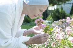 Svag sjuk hög kvinna som luktar blommor under oncologybehandling i trädgården royaltyfria bilder Svag sjuk hög kvinna som luktar blommor under oncologybehandling i trädgården royaltyfria bilder