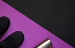 Svarta gymnastikskor och metallflaska på violett och svart geometriskt utrymme för bakgrundswhithkopia royaltyfri bild Svarta gymnastikskor och metallflaska på violett och svart geometriskt utrymme för bakgrundswhithkopia royaltyfri bild