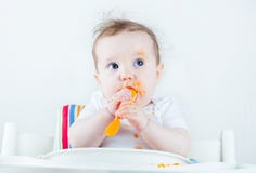 Sweet messy baby eating a carrot in a white high chair stock image Sweet messy baby eating a carrot in a white high chair stock image