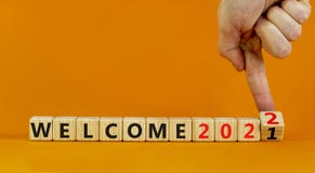 Symbol of planning 2022 welcome new year. Businessman turns a wooden cube and changes words `welcome 2021` to `welcome 2022`.