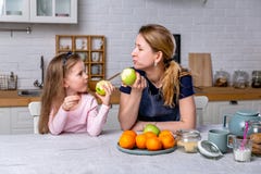 Szcz??liwa ma?a dziewczynka i jej pi?kna potomstwo matka ?niadanie wp?lnie w bia?ej kuchni Maj? zabaw? i jedz? jab?ka zdjęcie stock Szcz??liwa ma?a dziewczynka i jej pi?kna potomstwo matka ?niadanie wp?lnie w bia?ej kuchni Maj? zabaw? i jedz? jab?ka zdjęcie stock