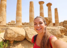 Szczęśliwa uśmiechnięta kobieta bierze jaźń portret z grecką świątynią na tle w dolinie świątynie przy Agrigento, Włochy fotografia stock Szczęśliwa uśmiechnięta kobieta bierze jaźń portret z grecką świątynią na tle w dolinie świątynie przy Agrigento, Włochy fotografia stock