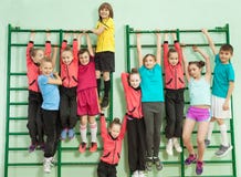 Szczęśliwi dzieciaki wiesza na ściennych barach w szkolnym gym obraz stock Szczęśliwi dzieciaki wiesza na ściennych barach w szkolnym gym obraz stock