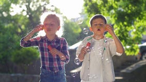 Szczęśliwy dzieciństwo, dziewczyna i chłopiec dmucha mydlanych bąble przy parkiem bawić się w świeżym powietrzu w backlight, zbiory wideo Szczęśliwy dzieciństwo, dziewczyna i chłopiec dmucha mydlanych bąble przy parkiem bawić się w świeżym powietrzu w backlight, zbiory wideo
