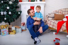 Szczęśliwy ojciec i jego syn blisko choinki z prezentem w domu fotografia stock Szczęśliwy ojciec i jego syn blisko choinki z prezentem w domu fotografia stock
