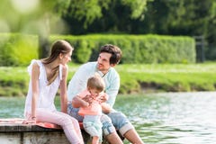 Szczęśliwy rodzinny obsiadanie na jetty na jeziorze lub stawie zdjęcia stock Szczęśliwy rodzinny obsiadanie na jetty na jeziorze lub stawie zdjęcia stock
