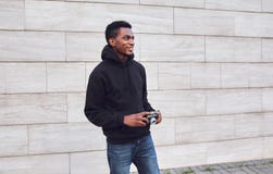 Szczęśliwy uśmiechnięty młody afrykański mężczyzna z rocznika filmu kamerą w czarnym hoodie odprowadzeniu na miasto ulicie obrazy royalty free Szczęśliwy uśmiechnięty młody afrykański mężczyzna z rocznika filmu kamerą w czarnym hoodie odprowadzeniu na miasto ulicie obrazy royalty free
