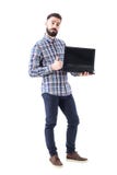 Szczęśliwy śmieszny brodaty facet z puste miejsce otwartego laptopu parawanowym pokazuje kciukiem up gest obraz stock Szczęśliwy śmieszny brodaty facet z puste miejsce otwartego laptopu parawanowym pokazuje kciukiem up gest obraz stock