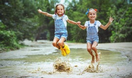 Szczęśliwy śmieszny siostra bliźniaków dziecka dziewczyny doskakiwanie na kałużach w pocieraniu Obrazy Royalty Free Szczęśliwy śmieszny siostra bliźniaków dziecka dziewczyny doskakiwanie na kałużach w pocieraniu Obrazy Royalty Free