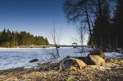 Słońca światło iluminował kamień przed zamarzniętym jeziorem z brzoz sosnami wokoło podczas gdy gałąź wiesza od niebieskiego nieb zdjęcia royalty free Słońca światło iluminował kamień przed zamarzniętym jeziorem z brzoz sosnami wokoło podczas gdy gałąź wiesza od niebieskiego nieb zdjęcia royalty free