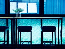 Tabourets de bar de silhouette et contre- barre en bois près du verre de fenêtre sur la pièce légère bleue photographie stock Tabourets de bar de silhouette et contre- barre en bois près du verre de fenêtre sur la pièce légère bleue photographie stock