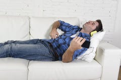 20-tal eller 30-talman som har gyckel som ligger på soffan som lyssnar till musik på mobiltelefonen med hörlurar som spelar Air G Fotografering för Bildbyråer 20-tal eller 30-talman som har gyckel som ligger på soffan som lyssnar till musik på mobiltelefonen med hörlurar som spelar Air G Fotografering för Bildbyråer