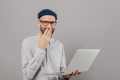 Talented male graphic designer works remotely on gadget, laughs positively, covers mouth with palm, wears spectacles and white royalty free stock photography Talented male graphic designer works remotely on gadget, laughs positively, covers mouth with palm, wears spectacles and white royalty free stock photography