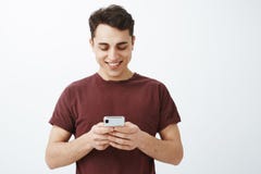 Talia strzał trzyma smartphone i ono uśmiecha się joyfully przy ekranem pozytywny życzliwy przystojny mężczyzna w czerwonej koszu obrazy stock Talia strzał trzyma smartphone i ono uśmiecha się joyfully przy ekranem pozytywny życzliwy przystojny mężczyzna w czerwonej koszu obrazy stock