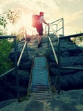 Tall backpacker hold handrail on rock. Sunny daybreak in rocks. Hiker with big backpack, baseball cap, dark pants and white shirt stock photos Tall backpacker hold handrail on rock. Sunny daybreak in rocks. Hiker with big backpack, baseball cap, dark pants and white shirt stock photos