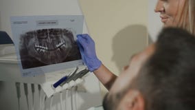 Tandläkare-kvinnan visar patienten en röntgenstråle för ytterligare behandling av tänderna dentistry Tandläkaren visar en ` s för stock video Tandläkare-kvinnan visar patienten en röntgenstråle för ytterligare behandling av tänderna dentistry Tandläkaren visar en ` s för stock video