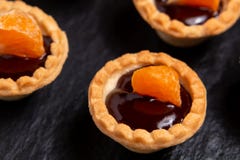 Tartelettes douces avec du chocolat et des tranches de mandarine sur un plat d'ardoise naturelle pour servir, plan rapproché photographie stock libre de droits Tartelettes douces avec du chocolat et des tranches de mandarine sur un plat d'ardoise naturelle pour servir, plan rapproché photographie stock libre de droits