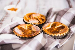 Tartlets взбрызнутые с напудренным сахаром с вареньем персика на белой деревянной предпосылке с полотенцем кухни стоковая фотография Tartlets взбрызнутые с напудренным сахаром с вареньем персика на белой деревянной предпосылке с полотенцем кухни стоковая фотография