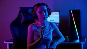 Tattooed gamer girl sitting by the PC and holding a lollipop