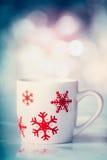 Taza blanca con los copos de nieve rojos en fondo del bokeh del invierno imágenes de archivo libres de regalías Taza blanca con los copos de nieve rojos en fondo del bokeh del invierno imágenes de archivo libres de regalías
