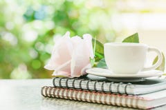 Taza del café con leche en los cuadernos espirales con la flor dulce de la rosa del rosa foto de archivo Taza del café con leche en los cuadernos espirales con la flor dulce de la rosa del rosa foto de archivo