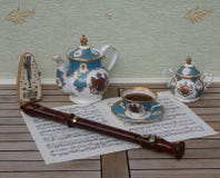 Tazza da the inglese con il piattino, ciotola di zucchero e della teiera, metronomo per musica e una flauto del blocco su uno str fotografie stock libere da diritti Tazza da the inglese con il piattino, ciotola di zucchero e della teiera, metronomo per musica e una flauto del blocco su uno str fotografie stock libere da diritti