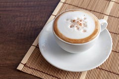 Tazza di caffè di cappuccino sulla stuoia di bambù, su spirito di legno del fondo fotografia stock Tazza di caffè di cappuccino sulla stuoia di bambù, su spirito di legno del fondo fotografia stock