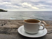 Tazza di caffè su una tavola di legno con una vista di oceano fotografia stock Tazza di caffè su una tavola di legno con una vista di oceano fotografia stock