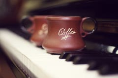 Tazza di caffè su una vecchia tastiera di piano mentre componendo Tempo di sera ed alcuni raggi del sole Tazza da caffè sulla tas Fotografie Stock Tazza di caffè su una vecchia tastiera di piano mentre componendo Tempo di sera ed alcuni raggi del sole Tazza da caffè sulla tas Fotografie Stock