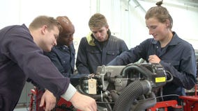 Teacher And Students In Car Mechanic Class Working On Engine