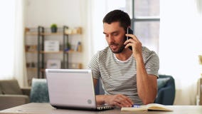 Man with laptop calling on phone at home office