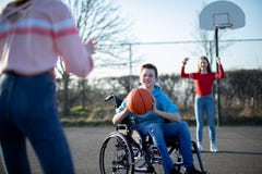 Teenage Boy In Wheelchair Playing Basketball With Friends