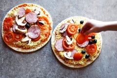 Teenage girl`s hand putting slice of tomato on raw pizza royalty free stock images Teenage girl`s hand putting slice of tomato on raw pizza royalty free stock images