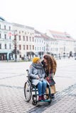 A teenager girl with disabled grandmother in wheelchair outdoors on the street in winter. royalty free stock photos A teenager girl with disabled grandmother in wheelchair outdoors on the street in winter. royalty free stock photos