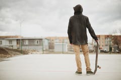 Teenager Standing In A Black Hoodie Holding A Hand Skateboard On The Background Urban Slum Stock Photo