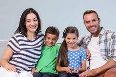 Televisione di sorveglianza della giovane famiglia felice con i loro due bambini fotografia stock Televisione di sorveglianza della giovane famiglia felice con i loro due bambini fotografia stock