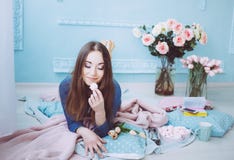Tender girl lying on the floor, eating macarons. Tulip flowers on the blue wall background in the spring morning royalty free stock photography Tender girl lying on the floor, eating macarons. Tulip flowers on the blue wall background in the spring morning royalty free stock photography
