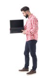 Tenuta barbuta dell'uomo di affari casuali astuti ed esaminare lo schermo in bianco del computer portatile immagine stock Tenuta barbuta dell'uomo di affari casuali astuti ed esaminare lo schermo in bianco del computer portatile immagine stock