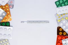 Termometro su un fondo bianco fra le pillole dei colori differenti in pacchetti immagini stock Termometro su un fondo bianco fra le pillole dei colori differenti in pacchetti immagini stock