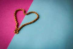 Textuur van het mooie gouden feestelijke ketting unieke weven in de vorm van een hart op een roze purpere blauwe ruimte als achte royalty-vrije stock afbeeldingen Textuur van het mooie gouden feestelijke ketting unieke weven in de vorm van een hart op een roze purpere blauwe ruimte als achte royalty-vrije stock afbeeldingen