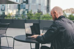 Thinking attractive adult successful bald bearded man in black jacket with laptop in street cafe at city stock photography Thinking attractive adult successful bald bearded man in black jacket with laptop in street cafe at city stock photography