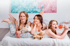 Three cute young girls sedyat on the bed in the room, are holdin Stock Photos Three cute young girls sedyat on the bed in the room, are holdin Stock Photos