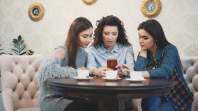 Three friends sitting in a cafe with a smart phone and having a funny conversation. Good girls with long beautiful black stock video footage Three friends sitting in a cafe with a smart phone and having a funny conversation. Good girls with long beautiful black stock video footage