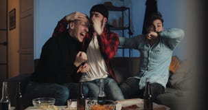 Three friends watching football match on tv at home, cheering best soccer team. Emotion. Mens fans celebrate winning. stock video footage Three friends watching football match on tv at home, cheering best soccer team. Emotion. Mens fans celebrate winning. stock video footage