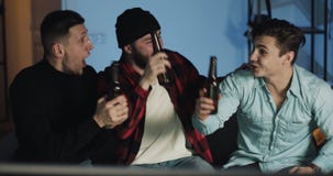 Three friends watching football match on tv at home, cheering best soccer team. Emotion. Mens fans celebrate winning. stock footage Three friends watching football match on tv at home, cheering best soccer team. Emotion. Mens fans celebrate winning. stock footage