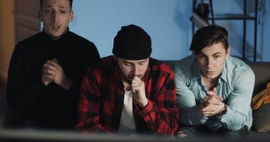 Three friends watching sport game on tv, worrying about team losing. Guys sitting on the sofa at home with beer and stock footage Three friends watching sport game on tv, worrying about team losing. Guys sitting on the sofa at home with beer and stock footage